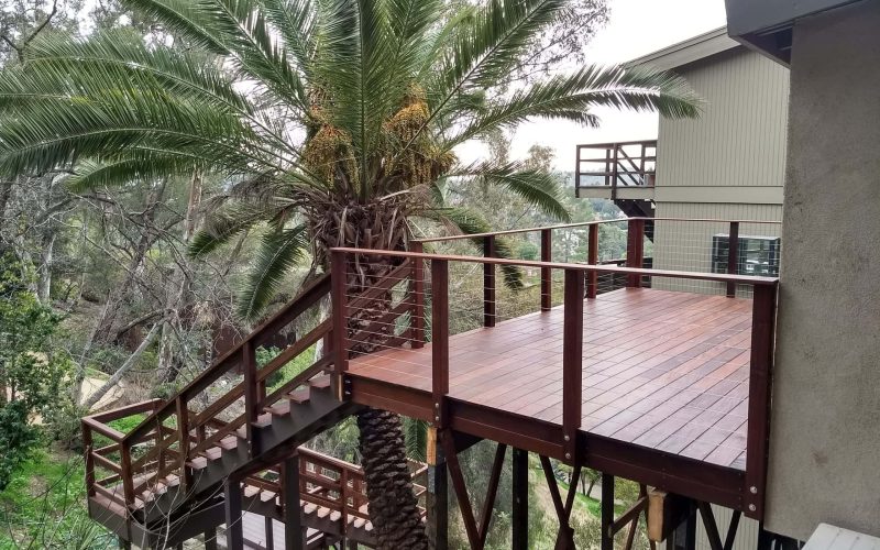 Deck extension featuring a wooden deck and railing around a tall palm tree in a residential backyard.